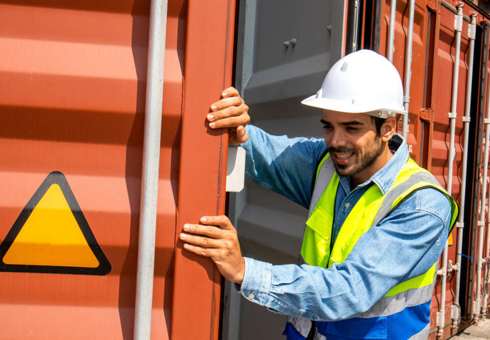 Ein Arbeiter mit Helm und Warnweste öffnet einen roten Überseecontainer, um den Lagercontainer zu sichern.