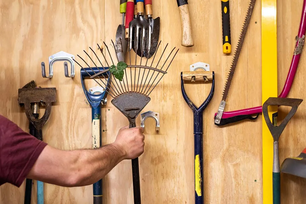 Ein Bild mit einer Wand an der Werkzeuge für den Garten hängen.
