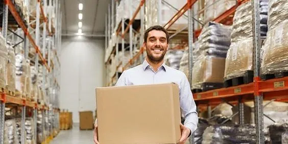 wholesale, logistic, business, export and people concept - happy man with cardboard parcel box at warehouse