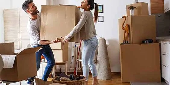 Young Couple Carrying Big Cardboard Box At New Home.Moving House