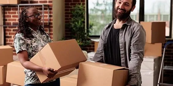 Portrait of diverse life partners posing with boxes on moving day, unpacking furniture and things to decorate rented apartment flat. Using cargo storage to settle in property bought on loan.