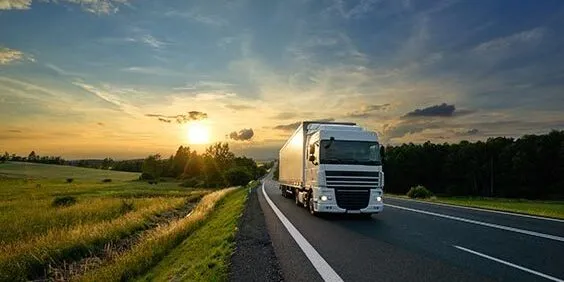 White truck driving on the asphalt road in rural landscape at sunset