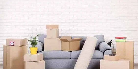 Cardboard boxes with household stuff and grey sofa on brick wall background